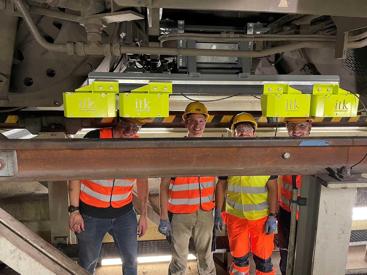 Experts from ITK and KIT stand under a locomotive behind the installed MAROS sensor